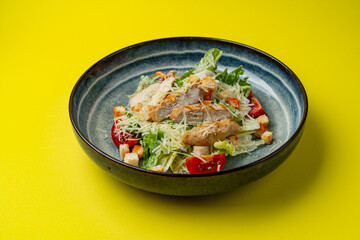 Caesar salad with chicken in a plate on a yellow background