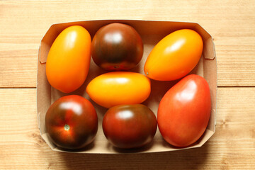 Yellow and red plum tomatoes in a cardboard box on a wooden table. View from above