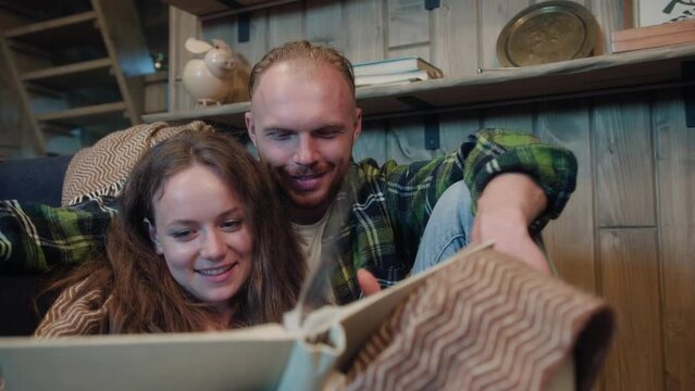 Happy couple sits and scrolls photo album in cozy house