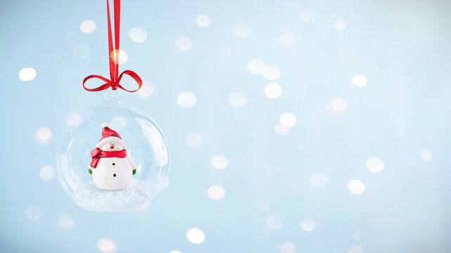 Transparent christmas bauble with snowman inside. Stock image with copy space and defocused bokeh on background