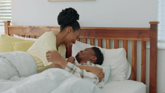 African couple, kiss in bed and happy relax together bonding in morning hotel bedroom under blankets. Young husband and wife smile, care and happiness while kissing with love on vacation or honeymoon