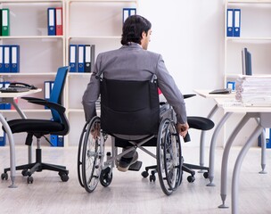 Young handsome employee in wheelchair working in the office