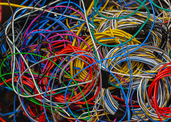 Colored telecommunication cables and wires tangled in a tangle in a box. The multicolored wires and cables in the box are mixed up and tangled into knots.