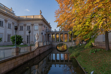 Fototapeta na wymiar a beautiful view of the palace with a bridge where the water flows trees with yellow leaves on the background of the blue sky the bridge is reflected in the water the palace in Lazienki Warsaw