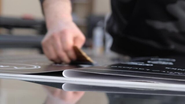 Advertising image printing paste. The man applying the vinyl printing foil to the material surface using a felt squeegee. 
