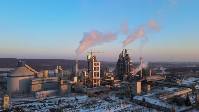 Aerial view of cement plant production area with high concrete factory structure and tower cranes at industrial site. Greenhouse gas smoke polluting air. Manufacture and global industry concept