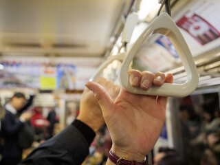 Hands holding on to handles to support themselves while standing on a busy subway train - 540136946