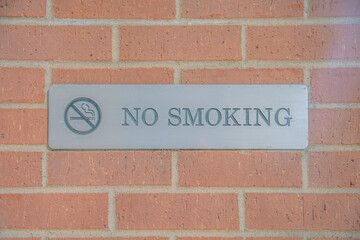 No Smoking sign debossed on a metal plate against brick wall of a building