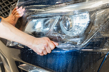 The process of installing PPF film on the headlight of the car. Selective, blurred focus. The...
