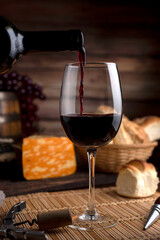 glass of red wine on wooden table with bread and cheese, bottle opener and background wooden barrel...