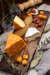 table with varieties of cheese brie camembert cheddar parmesan cheese with bell peppers on a wooden board adorned with dried flowers oil and pepper shaker