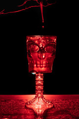 copa de calavera medio llena con agua y mano dejando caer gotas en el interior retroiluminada de rojo
