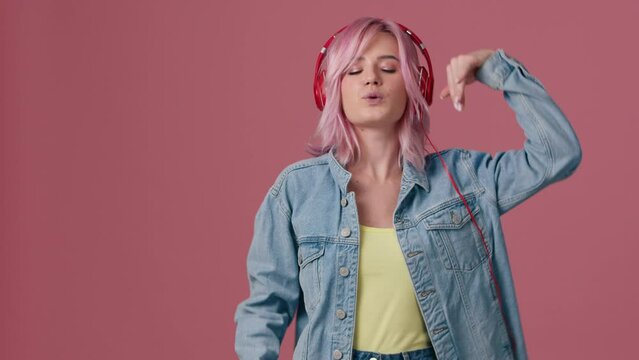 Young woman with colorful hairstyle dancing on pink background. Female having fun when listening music. 20s model smiling, pink hair flutter beautifully. Girl moves to rhythm of music positive footage