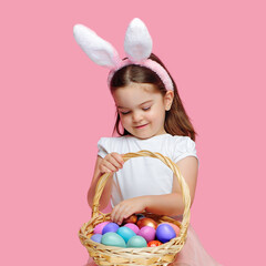 Pretty little girl wearing Easter bunny ears looking into her basket with eggs