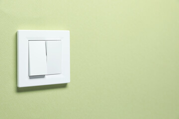 Modern plastic light switch on green background. Space for text
