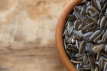 Bowl with organic sunflower seeds on wooden table, top view. Space for text