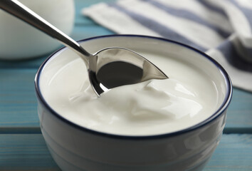 Eating tasty yogurt from bowl on light blue wooden table, closeup