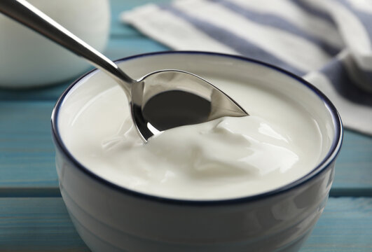 Eating tasty yogurt from bowl on light blue wooden table, closeup