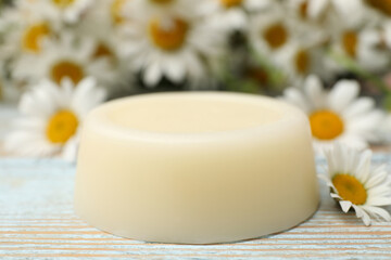 Obraz na płótnie Canvas Solid shampoo bar and chamomiles on light wooden table, closeup. Hair care