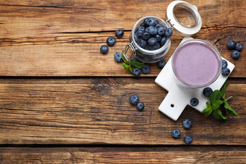 Glass of blueberry smoothie with mint and fresh berries on wooden table, flat lay. Space for text