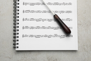 Conductor's baton and sheet music book on grey background