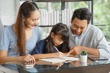 Obraz premium Children education and home school concept : Young asian father and mother see little daughters' study. Excited smiling small child girl enjoying learning and writing with pleasant dad and mom at home