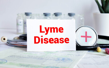On a light wooden table there is a stethoscope, a pen and a sheet of paper with the text LYME DISEASE.