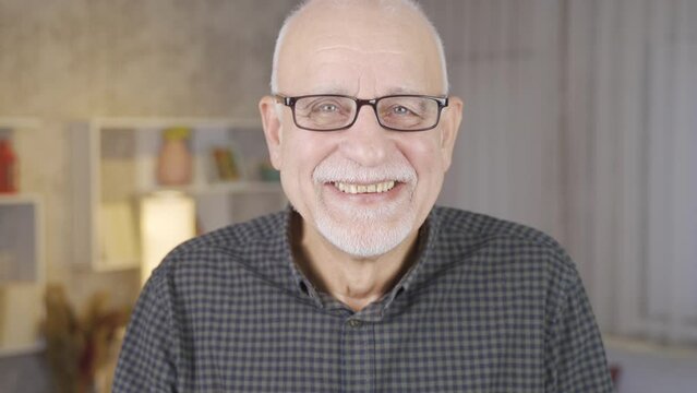 Cute old grandfather waving and babbling looking at camera.
Old man waving while looking at camera making cute gestures.
