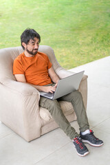Latin man working from his garden on his laptop sitting on a sofa