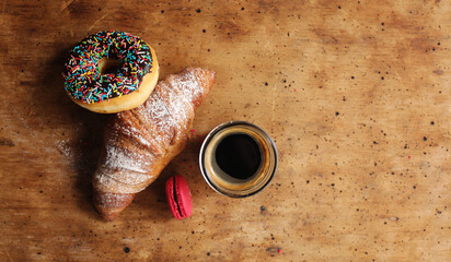 Cup of coffee, croissant, donuts and macaroons on wooden background. Vintage background.