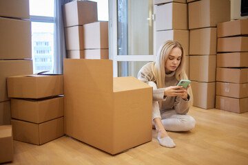 Young woman moving new place and repair concept - happy young woman with many cardboard boxes sitting on floor at home.