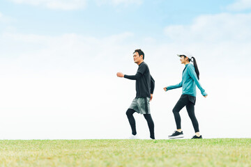 青空の見える公園を健康のためウォーキングしてダイエットしている男女
