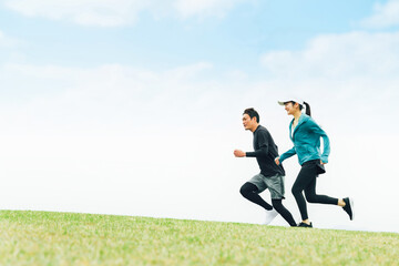 青空の見える公園でランニングするスポーツウェアを着たアジア人の男女（走る）

