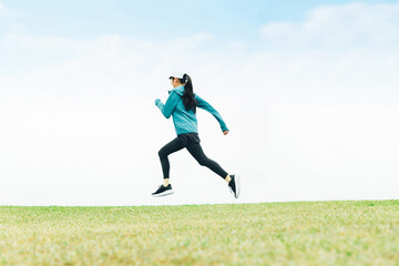 草原をジャンプしながら走るスポーツウェアのアジア人女性
