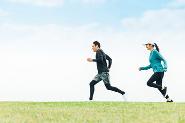 Fototapeta na wymiar 青空の見える公園でランニングするスポーツウェアを着たアジア人の男女（走る） 