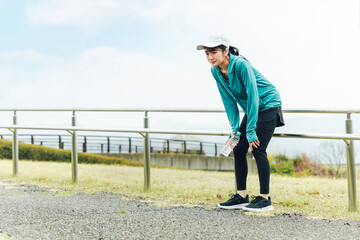 風邪をひいて体調不良で倦怠感を感じながら有酸素運動するランナーのアジア人女性
