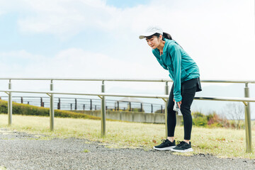 運動中に呼吸困難・喘息・息切れで苦しくて困るスポーツウェアのアジア人女性
