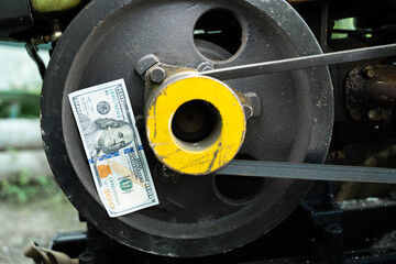 A hundred dollar bill stuck to a tractor pulley close-up. Money and the agricultural industry. The cost of cultivation and tillage. Maintenance of agricultural machinery
