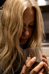 young blonde woman looking at a crystal glass with red wine.