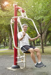 happy senior man with grey hair doing exercise on outdoor fitness equipment in the city park