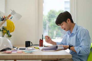 Side view of smiling young  architect in shirt working on blueprints at bright  modern office.