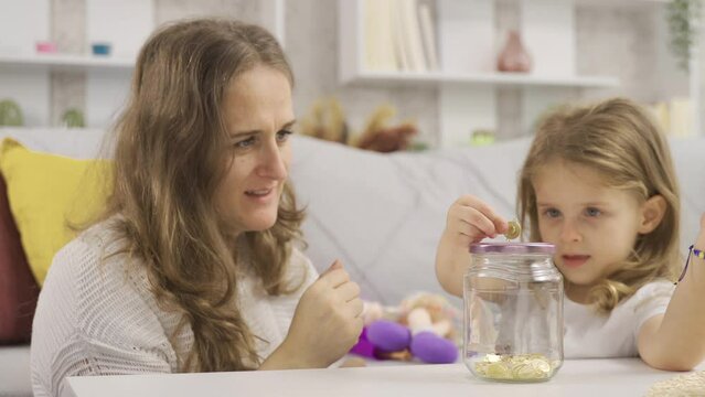 Gold is being thrown into her little girl's piggy bank for her future.
Caring parent teaches kid to save money, think about future, manage personal finance, savings concept.
