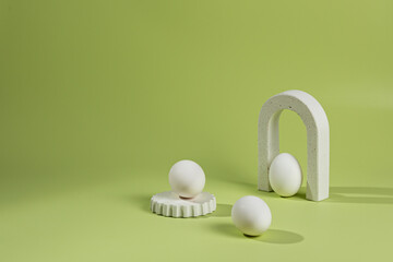 Composition on a green background of white podiums and arches with chicken eggs with a shadow from sunlight