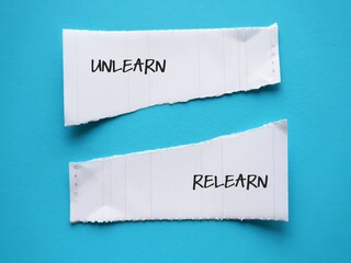 Torn note paper on blue background with handwritten text Unlearn and Relearn - knowing to discard...