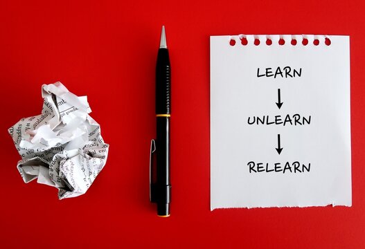 Pen ,crumpled paper and note paper on red background with handwritten text Learn Unlearn Relearn - concept of knowing to discard learned outdated knowledge skills fake information and relearn new ones