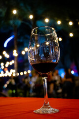 Copa de cristal con poco vino tinto con fiesta de fondo