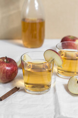 Two glasses with apple cider or juice on a light background, apples in pieces, a white cloth nearby
