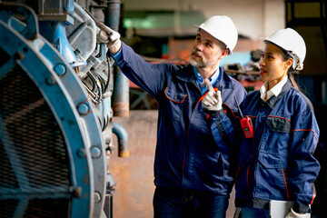 Caucasian factory man point to machine and explain about the funtion and the problem of machine to his Asian coworker in industrial workplace area.