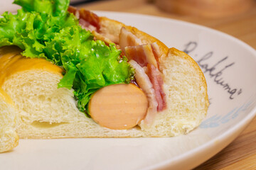 Hotdog with bacon and sausage on white plate
