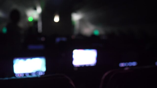 Blurred view of dark cabin of airliner, overnight flight, clip includes original audio, noise of aircraft engines. Some passengers watch movies with entertainment system, displays built into all seats